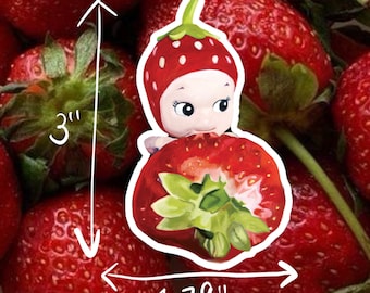 May include: A ceramic figurine of a strawberry with a human face, wearing a red strawberry hat. The figurine is holding a strawberry in its hands. The figurine is 3 inches tall and 1.79 inches wide.