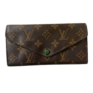May include: Brown leather wallet with a flap closure and a green button. The wallet features a repeating pattern of brown logos. The wallet is rectangular and appears to be made of high-quality leather.