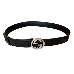 May include: Black leather belt with a silver-tone buckle featuring a double G logo. The belt is a classic accessory, suitable for various outfits. The buckle is a prominent design element.