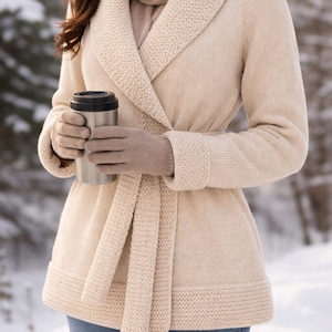 Könnte beinhalten: Ein cremefarbener Strickcardigan mit Schalkragen und passendem Bindegürtel. Der Cardigan wird mit einem beigen Schal und Handschuhen getragen. Ein Edelstahl-Reisebecher wird in den Händen gehalten. Der Hintergrund ist eine verschneite Szene im Freien.