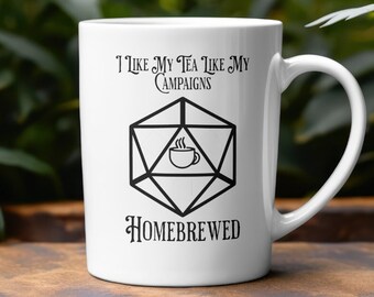 May include: White ceramic mug with a black graphic of a twenty-sided die with a teacup inside. The text reads "I like my tea like my campaigns homebrewed".