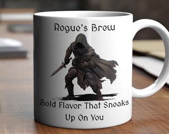 May include: White ceramic mug with a black and white illustration of a hooded figure holding a sword. The text "Rogue's Brew" is printed above the illustration and "Bold Flavor That Sneaks Up On You" is printed below.