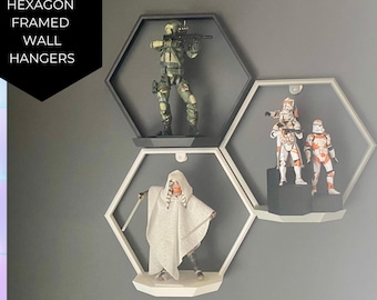 Puede incluir: Tres estantes hexagonales de pared con marcos blancos y estantes negros. Los estantes están montados en una pared gris y muestran figuras de acción. El estante superior tiene una figura de acción verde con una pistola. El estante del medio tiene dos figuras de acción blancas con acentos naranjas. El estante inferior tiene una figura de acción blanca con una capa blanca.
