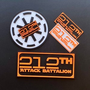 Op de afbeelding: Drie zwarte en oranje stickers met de tekst "212th Attack Battalion". De stickers zijn op een zwarte achtergrond.