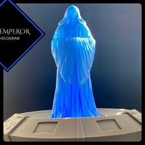 May include: A blue hologram of a figure in a hooded robe, standing on a round, white base. The hologram is labelled "THE EMPEROR 6" HOLOGRAM".