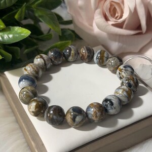 May include: A beaded bracelet featuring round, polished stones in shades of blue, brown, and white. The bracelet is strung on a clear elastic cord. The stones have a marbled appearance.