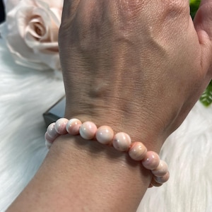 May include: A pink beaded bracelet with round beads. The bracelet is made of light pink and white beads. The bracelet is worn on a wrist.