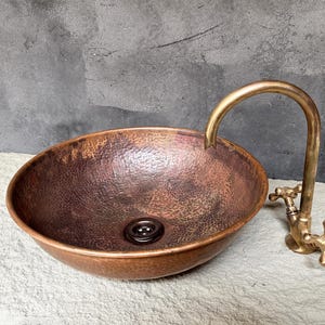 K&ouml;nnte beinhalten: Ein geh&auml;mmertes Kupferwaschbecken mit einem Messinghahn. Das Waschbecken hat ein rustikales, gealtertes Aussehen und ist perfekt f&uuml;r ein modernes Badezimmer.