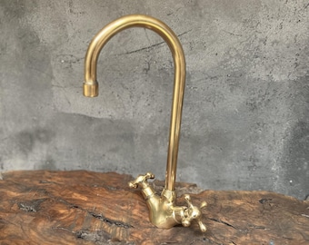 May include: A gold-toned faucet with a curved spout and two handles. The faucet is mounted on a wooden surface.