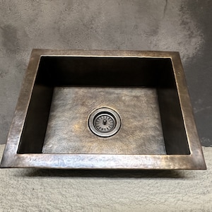 May include: A rectangular, hammered copper kitchen sink with a single drain.