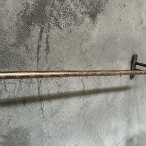May include: A rustic, hammered copper towel bar with a simple design. The bar is mounted to a wall with two brackets.