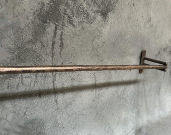 Könnte beinhalten: Eine rustikale, gehämmerte Kupfer-Handtuchhalterung mit schlichtem Design. Die Stange ist mit zwei Halterungen an einer Wand befestigt.