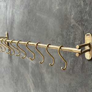 May include: Gold metal kitchen rack with 12 hooks. The rack is mounted to a wall and has a curved design.