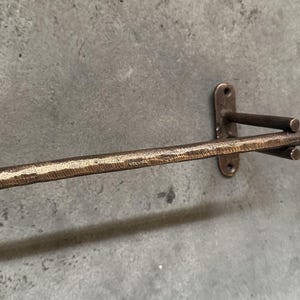 May include: A bronze towel rack with a hammered finish. The rack is mounted to a wall and has a single bar.