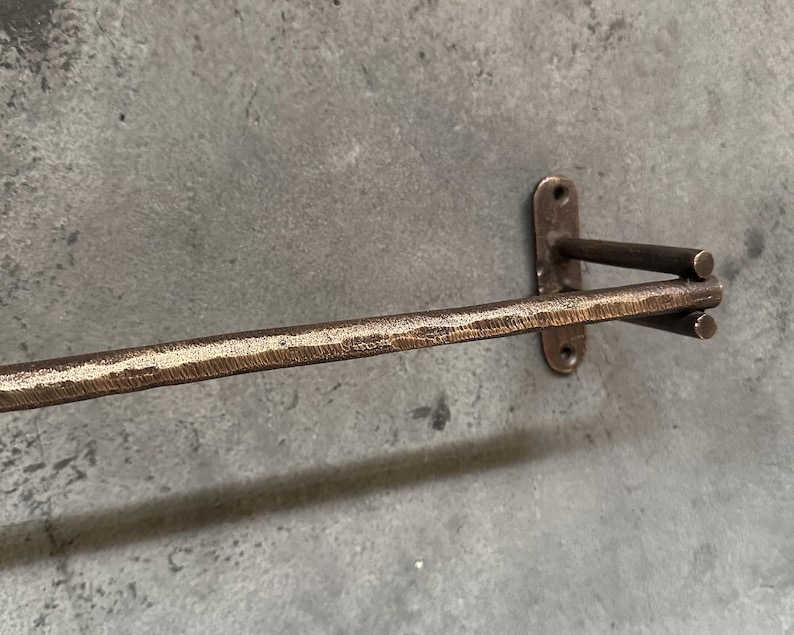 May include: A bronze towel rack with a hammered finish. The rack is mounted to a wall and has a single bar.