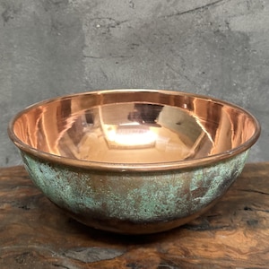 May include: A copper bowl with a green patina finish. The bowl is round and has a smooth, shiny surface.