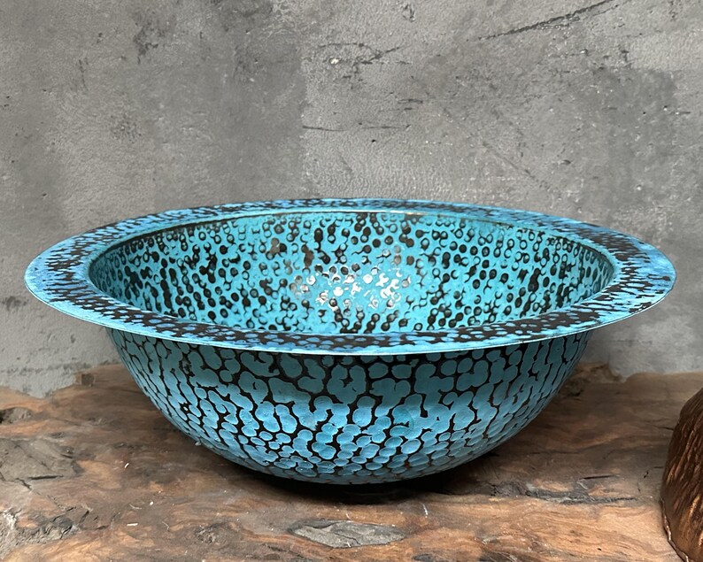 May include: A turquoise bowl with a textured surface and a black dotted pattern. The bowl has a wide rim and is set on a wooden surface. The bowl's interior is a lighter shade of turquoise.