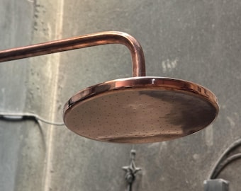 Könnte beinhalten: Ein Duschkopf aus Kupfer mit einem runden, flachen Design und einem Sprühmuster aus kleinen Löchern. Der Duschkopf ist an einem Kupferrohr befestigt.