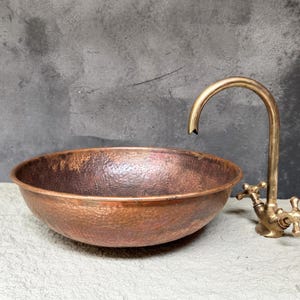 K&ouml;nnte beinhalten: Ein geh&auml;mmertes Kupfer-Waschbecken mit einem Messinghahn. Das Waschbecken hat ein rustikales, gealtertes Aussehen und ist perfekt f&uuml;r ein modernes Badezimmer.