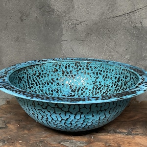 May include: A turquoise ceramic bowl with a speckled pattern. The bowl has a wide, rounded rim and a textured surface. The interior and exterior are a vibrant turquoise colour with black speckles, creating a unique design.