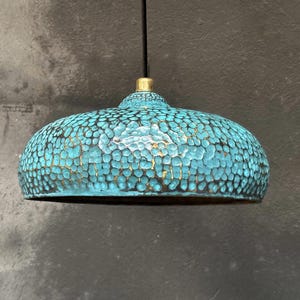 May include: A turquoise blue pendant light with a hammered metal finish. The light has a round, dome-shaped shade with a gold-colored top.