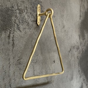 May include: Gold triangular towel rack with a wall mount. The rack is made of metal and has a simple, modern design.