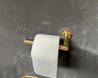 May include: Gold metal paper towel holder mounted on a gray wall. A white paper towel is hanging from the holder.