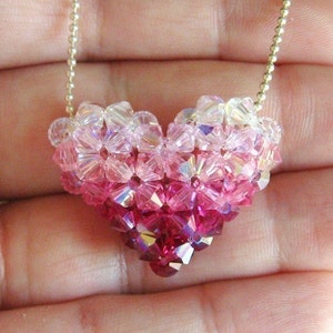 May include: A heart-shaped pendant necklace made of pink and clear crystal beads. The beads are arranged in a gradient pattern, starting with clear beads at the top and transitioning to pink beads at the bottom.