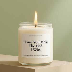May include: A lit soy wax candle in a clear glass jar. The candle has a white label with the text "I Love You More. The End. I Win." The candle is hand-poured and eco-friendly.