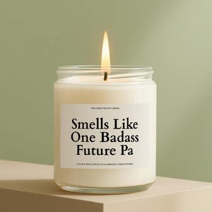 May include: A lit white soy wax candle in a clear glass jar. The label reads "Smells Like One Badass Future Pa". The candle is hand-poured and eco-friendly.