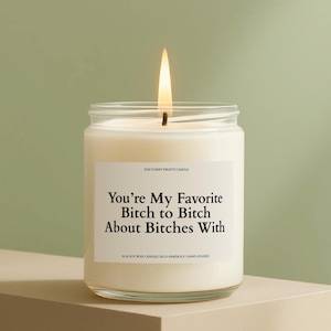 A white candle with a lit flame sits on a beige surface against a green background.
