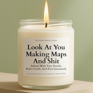 May include: A clear glass jar candle filled with white wax and a lit wick. The white label features black text reading: THE STARRY NIGHTS CANDLE, Look At You Making Maps And Shit, Infused With Tiny Details, Perfect Grids, And Zero Guesswork, %100 SOY WAX CANDLE | ECO-FRIENDLY | HAND-POURED.