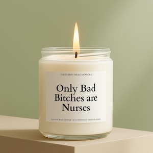 May include: A lit, white candle in a clear glass jar. The label reads "Only Bad Bitches are Nurses." The candle is on a beige surface against a green background. The text "THE STARRY NIGHTS CANDLE" is above the main text.
