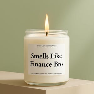 May include: A lit, white candle in a clear glass jar. The label reads "Smells Like Finance Bro" with "The Starry Nights Candle" above and "100% Soy Wax Candle | Eco-Friendly | Hand-Poured" below. The candle sits on a beige surface.