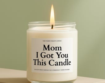Może przedstawiać: Zapalone świeca w przezroczystym szklanym słoiku z białą etykietą z napisem "Mom I Got You This Candle". Świeca stoi na beżowej powierzchni na zielonym tle. Tekst "The Starry Nights Candle" znajduje się powyżej.