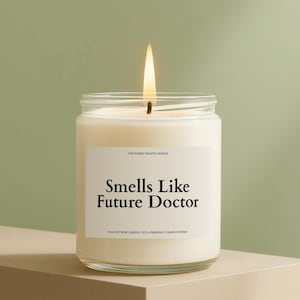 May include: A lit, white soy wax candle in a clear glass jar. The label reads "Smells Like Future Doctor." The candle is hand-poured and eco-friendly. The background is a light green.