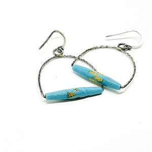May include: A pair of silver hoop earrings with a light blue glass bead accented with gold flecks.