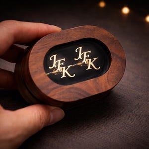 May include: A white ceramic mug with a black handle and the text "But First, Coffee" in a bold, black font. The mug is set against a blurred background, highlighting its clean design.