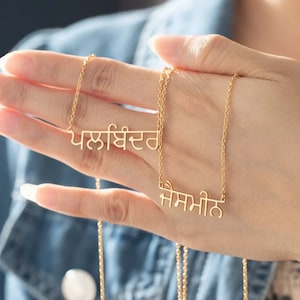Op de afbeelding: Twee gouden kettingen met een delicate ketting. De kettingen hebben een hanger met de woorden "ਪਲਾਂਬਿਹਤਰ" en "ਸੰਸਮੀਤ" in Gurmukhi-schrift.