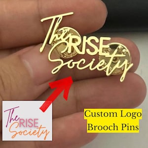 Puede incluir: Broche dorado con el texto "The RISE Society" en cursiva. El broche es un diseño de logotipo personalizado. La imagen también incluye un gráfico más pequeño del logotipo y el texto "Custom Logo Brooch Pins".