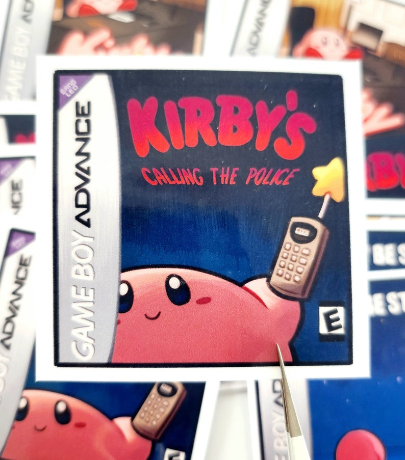 Peut inclure: Un autocollant repr&eacute;sentant une cartouche de jeu vid&eacute;o pour Game Boy Advance. L'autocollant pr&eacute;sente un personnage rose tenant un t&eacute;l&eacute;phone avec le texte "KIRBY'S CALLING THE POLICE" en lettres rouges.