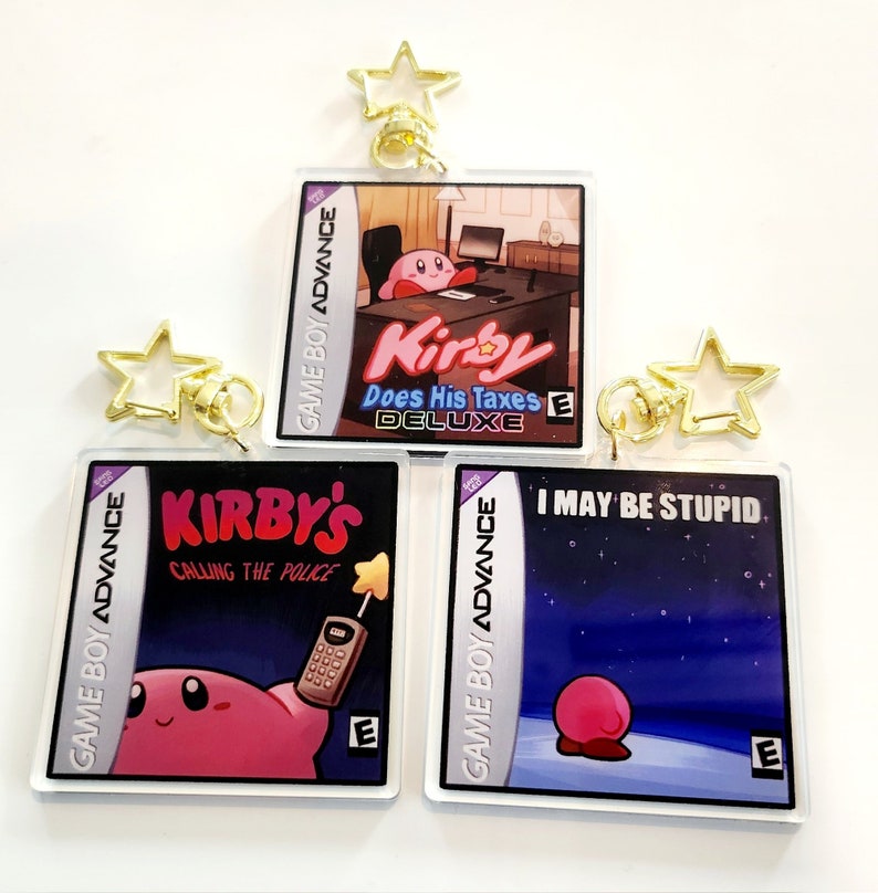 Peut inclure: Trois porte-cl&eacute;s de cartouche de jeu Game Boy Advance repr&eacute;sentant Kirby. Le premier porte-cl&eacute;s montre Kirby assis sur une chaise de bureau rose, &agrave; un bureau avec un ordinateur. Le texte sur le porte-cl&eacute;s est "Kirby Does His Taxes Deluxe". Le deuxi&egrave;me porte-cl&eacute;s montre Kirby tenant un t&eacute;l&eacute;phone portable avec le texte "Kirby's Calling the Police". Le troisi&egrave;me porte-cl&eacute;s montre Kirby debout sur un fond bleu avec des &eacute;toiles, avec le texte "I May Be Stupid".