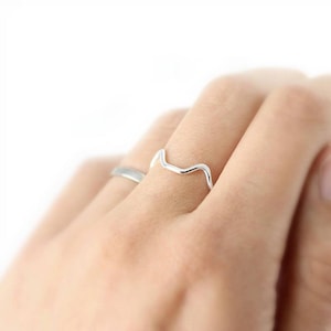May include: A silver ring with a wavy design. The ring is on a person's finger.