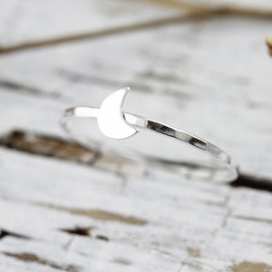 May include: A silver ring featuring a crescent moon design. The ring is thin and delicate, with a hammered finish.