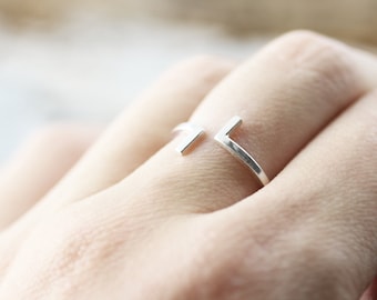 May include: A silver ring with a geometric design. The ring is open and has two straight lines that intersect at a right angle.