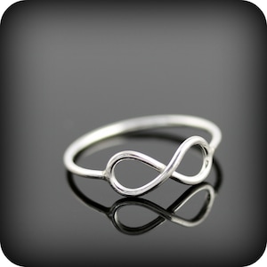 May include: A silver infinity ring with a simple design. The ring is on a black background.