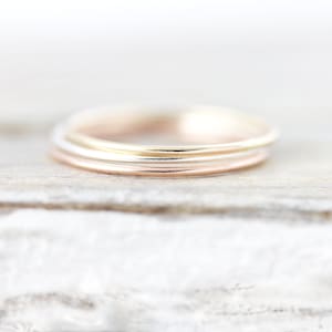 Peut inclure: Un ensemble de trois bagues fines et lisses à empiler, déclinées en différentes teintes métalliques, notamment l'or jaune, l'or rose et l'argent. Chaque bague présente un design simple, rond et poli, sans ornements ni pierres visibles.