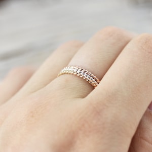 May include: A set of three thin gold rings with a textured, beaded design. The rings are stacked on top of each other.