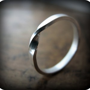 May include: A silver twisted band ring. The ring is made from a single piece of metal that is twisted into a unique shape.