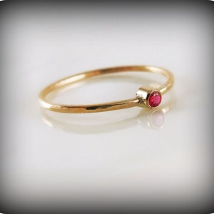 Peut inclure: Une bague simple en or avec une petite pierre rouge ronde.
